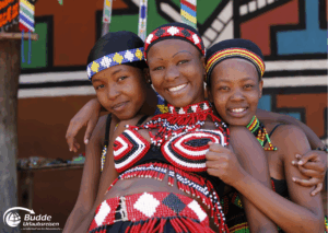 Kultur Urlaub Afrika: Drei Frauen in traditioneller afrikanischer Kleidung mit farbenfrohem Schmuck und lächelnden Gesichtern.