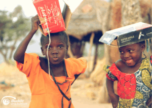 Kultur Urlaub Afrika: Zwei Kinder in Afrika tragen Kartonhüte und lächeln in die Kamera.