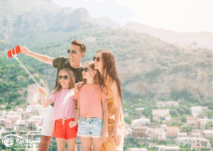 Urlaubsfoto: Familie posiert für ein Selfie mit einem Selfie-Stick in einer sonnigen Umgebung.