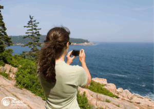 Urlaubsfoto: Eine Frau mit langen Haaren hält eine Kamera und fotografiert die Küste am Meer.