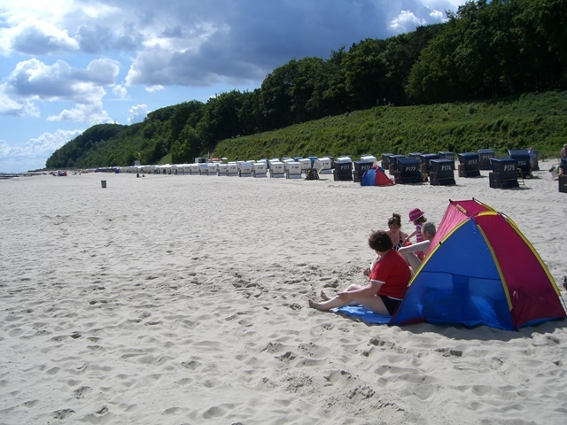 Familienurlaub-Ostsee-Babyreise-Usedom-Sandstrand Das entzückende Bild zeigt eine fröhliche Familie, die einen unvergesslichen Familienurlaub an der Ostsee auf der Insel Usedom verbringt. Sie haben sich einen wunderschönen Platz am endlosen Sandstrand gesichert. Das Baby spielt vergnügt im weichen Sand und die Eltern beobachten liebevoll, wie es die ersten Schritte im flachen Wasser unternimmt. Ein Familienurlaub auf Usedom bietet die perfekte Kulisse für erholsame Tage am Strand, gemeinsame Spaziergänge entlang der Küste und wertvolle Zeit miteinander. Buchen Sie jetzt Ihren Familienurlaub auf Usedom und genießen Sie unbeschwerte Tage am Ostseestrand.