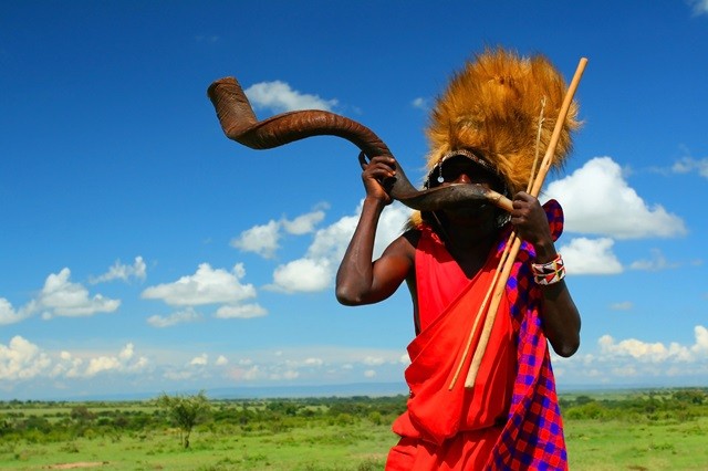 Massai-Krieger, der traditionelles Horn spielt. Afrika. Kenia. Masai Mara Das fesselnde Bild zeigt einen mutigen Massai-Krieger aus Kenia, der ein traditionelles Horn spielt. Die farbenfrohe Kleidung des Kriegers und seine stolze Haltung verleihen dem Bild eine authentische Atmosphäre. Das Horn, das er spielt, erzeugt einen kraftvollen Klang, der die Schönheit der afrikanischen Kultur widerspiegelt. Dieses Bild lädt den Betrachter ein, in die faszinierende Welt der Massai einzutauchen und die lebendige Kultur und Traditionen dieses faszinierenden Volkes zu entdecken. Erleben Sie die kraftvolle Energie und die fesselnde Musik der Massai-Krieger inmitten der atemberaubenden Landschaft der Masai Mara.