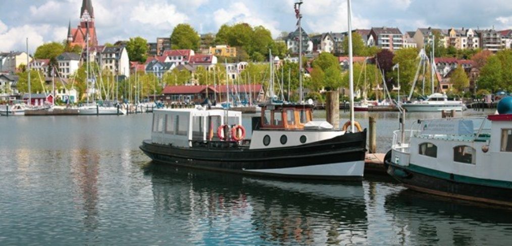 Barkasse Solitüde Schiff-Flensburg-Ostsee Ferienregion Das Bild zeigt die charmante Barkasse Solitüde, ein Schiff, das gemütliche Fahrten entlang der Ostseeküste in der Ferienregion Flensburg anbietet. Die Barkasse gleitet sanft über das ruhige Wasser und bietet den Passagieren eine entspannte Möglichkeit, die malerische Küstenlandschaft zu erkunden. Mit ihrem klassischen Design und ihrem freundlichen Personal ist die Solitüde ein beliebtes Schiff für Ausflüge und Entdeckungstouren. Auf dem Bild ist sie vor der Kulisse von Flensburg zu sehen, einer historischen Stadt, die für ihre maritimen Traditionen bekannt ist.