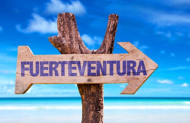 Fuerteventura-urlaubsreisen-Kanaren-Urlaub buchen Das Bild zeigt ein pittoreskes Schild am Strand von Fuerteventura, einer der atemberaubenden Kanarischen Inseln. Das Schild trägt den Schriftzug "Fuerteventura" und symbolisiert die Sehnsucht nach einem unvergesslichen Urlaub. Fuerteventura lockt mit endlosen Sandstränden, türkisblauem Wasser und ganzjährig mildem Klima. Ob Wassersport, Sonnenbaden oder Erkundungstouren durch die faszinierende Natur - Fuerteventura bietet für jeden Reisenden das perfekte Urlaubserlebnis.