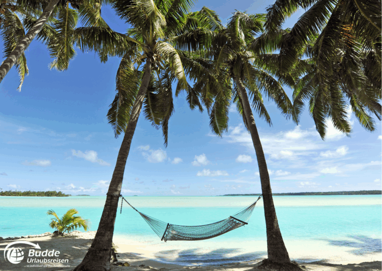 Urlaubsreise Paradies: Hängematte zwischen zwei Palmen an einem Strand mit türkisfarbenem Wasser im Hintergrund.