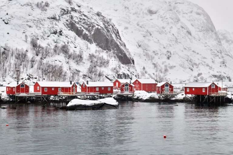 Urlaubsreisen Rote Fischerhäuser auf Stelzen am Wasser in einer winterlichen Landschaft in Norwegen.