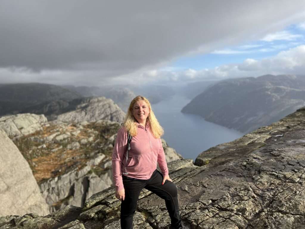 Anke Budde steht am Rande des Preikestolen in Norwegen und verkörpert die tiefgreifende Bedeutung des Reisens. Vor dem atemberaubenden Panorama der norwegischen Fjorde wird deutlich, wie das Reisen uns dazu inspiriert, unsere Grenzen zu überschreiten und die Schönheit der Welt zu erkunden.