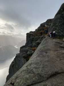 Gipfelblick vom Preikestolen Genießen Sie den atemberaubenden Blick vom Gipfel des Preikestolen. Das Bild zeigt Wanderer, die auf dem markanten Felsen stehen und den Blick über den Lysefjord schweifen lassen. Die Szene ist geprägt von der unberührten Schönheit der norwegischen Natur und bietet ein unvergleichliches Panorama, das Wanderer in seinen Bann zieht.