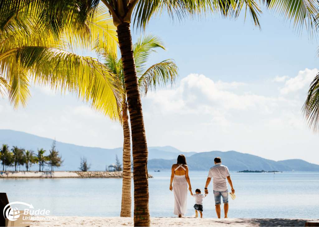 Familie spaziert Hand in Hand am Strand unter Palmen bei ihren Urlaubsreisen