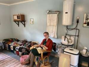 Eine Frau sitzt in einem historischen Wohnzimmer und strickt.