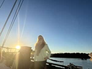 Anke Budde steht an Bord eines Bootes mit Sonnenuntergang im Hintergrund.