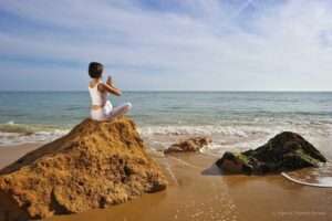 Eine Frau meditiert auf einem Felsen am Strand