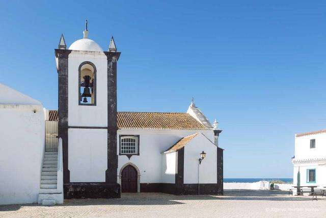 Eine historische Kirche mit weißer Fassade und einem Glockenturm in Cacela Velha, Algarve.