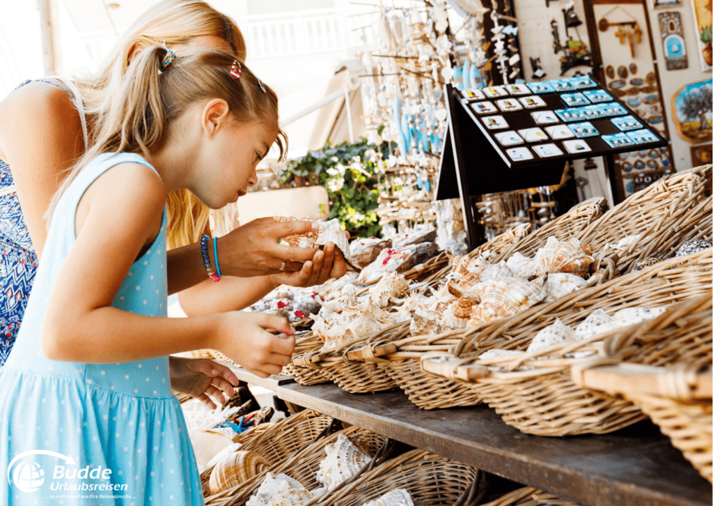 Souvenirs kaufen auf nachhaltiges Reisen. Eine Frau und ein Kind betrachten Muscheln und andere handgefertigte Waren auf einem Markt für nachhaltiges Reisen.