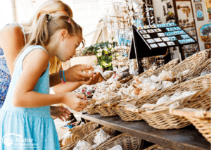 Souvenirs kaufen auf nachhaltiges Reisen. Eine Frau und ein Kind betrachten Muscheln und andere handgefertigte Waren auf einem Markt für nachhaltiges Reisen.