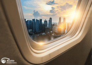 Blick aus einem Flugzeugfenster auf die Skyline einer Stadt bei Sonnenuntergang, ideal für eine Reise gegen Einsamkeit.