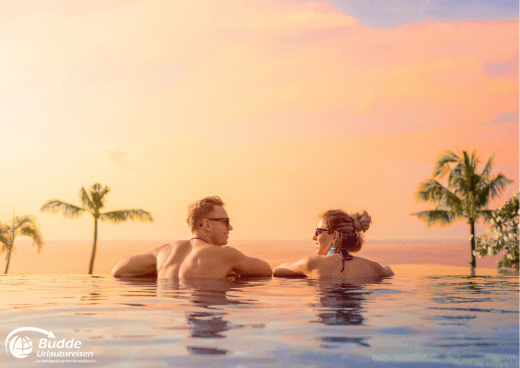 Flitterwochen Saint Martin - Ein Paar entspannt während der Urlaubsreisen in einem Infinity-Pool bei Sonnenuntergang. Reisen nach Saint Martin buchbar bei Budde Urlaubsreisen.