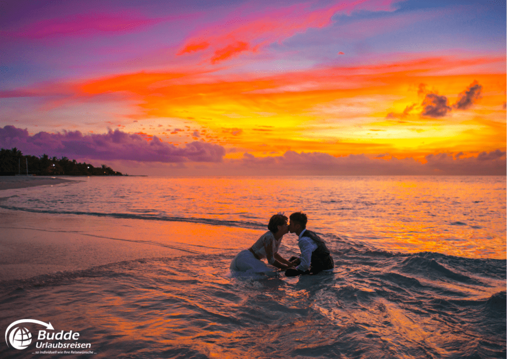 Flitterwochen Saint Martin - Ein Paar küsst sich im seichten Wasser bei Sonnenuntergang. Reisen nach Saint Martin buchbar bei Budde Urlaubsreisen.