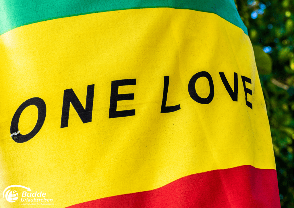 Urlaubsreisen Nahaufnahme einer Flagge mit dem Schriftzug 'One Love' in den Farben Gelb, Grün und Rot.