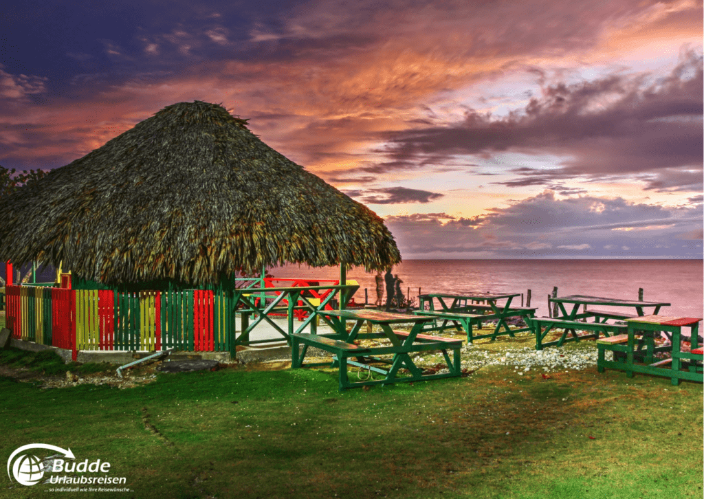 Urlaubsreisen Hütte mit Strohdach und Holztischen am Strand während eines Sonnenuntergangs.
