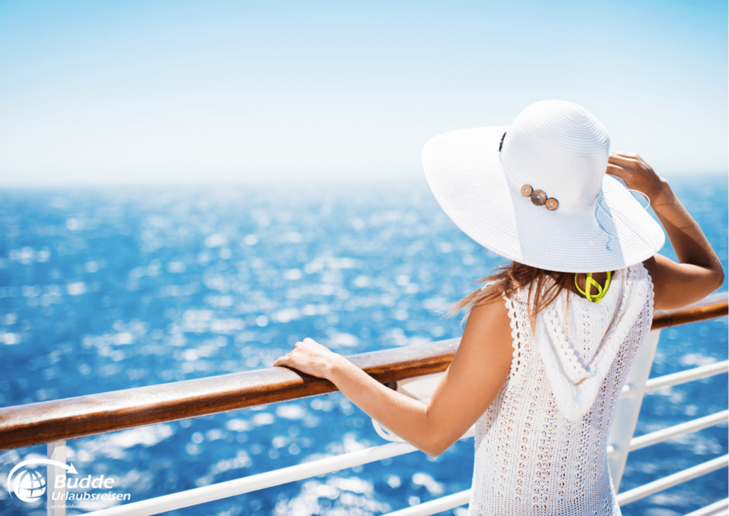 Urlaubsreisen Frau mit einem weißen Sonnenhut, die auf dem Deck eines Kreuzfahrtschiffs steht und auf das Wasser blickt.