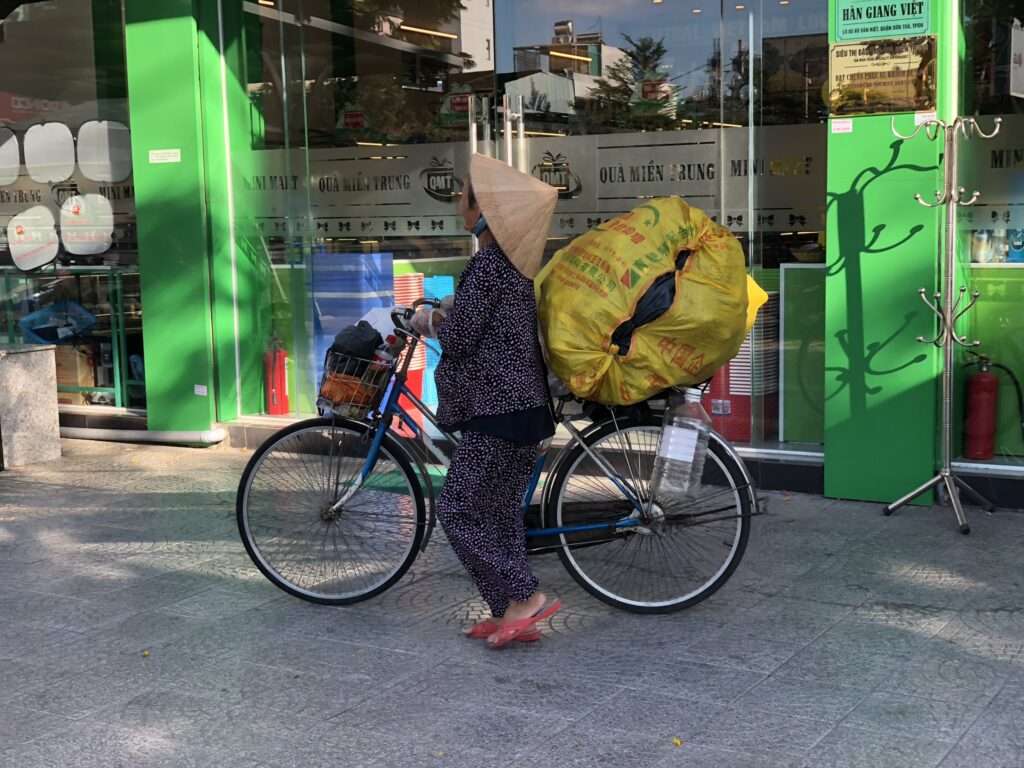 World Tourism Day 2024 - Frau mit traditionellem Hut fährt Fahrrad in Ho-Chi-Minh-Stadt, Vietnam.