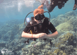 Ägypten Urlaub: Ein Junge mit Tauchausrüstung schwimmt unter Wasser im Roten Meer zwischen Korallen. - buchbar im Reisebüro Budde Urlaubseisen