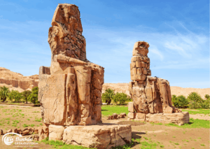 Ägypten Urlaub: Zwei massive Steinskulpturen der Kolosse von Memnon in Luxor, Ägypten, vor blauem Himmel. - buchbar im Reisebüro Budde Urlaubseisen