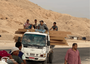 Ägypten Urlaub: Ein Chevrolet-Lkw transportiert Holzplatten mit mehreren Personen auf dem Dach in einer Wüstenlandschaft. - buchbar im Reisebüro Budde Urlaubseisen