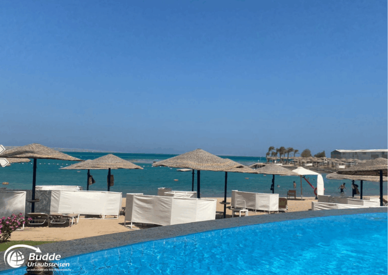 Ägypten Urlaub: Strand mit weißen Sonnenschirmen und Liegen am Wasser in Marsa Alam, Ägypten. - buchbar im Reisebüro Budde Urlaubseisen