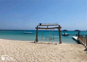 Ägypten Urlaub: Holzschaukel mit dem Schriftzug 'I love Eden Island' am Strand mit Booten im Hintergrund. - buchbar im Reisebüro Budde Urlaubseisen