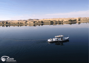 Ägypten Urlaub: Ein Boot fährt auf dem ruhigen Wasser des Nils mit sanften Hügeln im Hintergrund. - buchbar im Reisebüro Budde Urlaubseisen