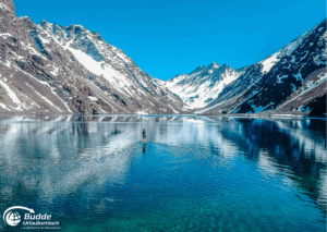 einzigartige Reiseerlebnisse weltweit: Ein Paddleboarder auf ruhigem Wasser in einem Gebirgssee in den Anden mit schneebedeckten Bergen im Hintergrund. - buchbar im Reisebüro Budde Urlaubseisen