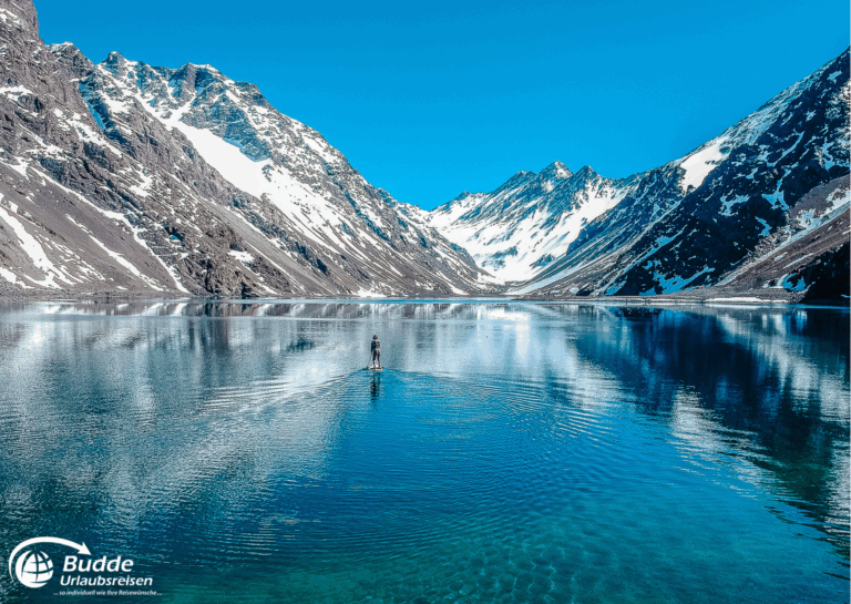 einzigartige Reiseerlebnisse weltweit: Ein Paddleboarder auf ruhigem Wasser in einem Gebirgssee in den Anden mit schneebedeckten Bergen im Hintergrund. - buchbar im Reisebüro Budde Urlaubseisen