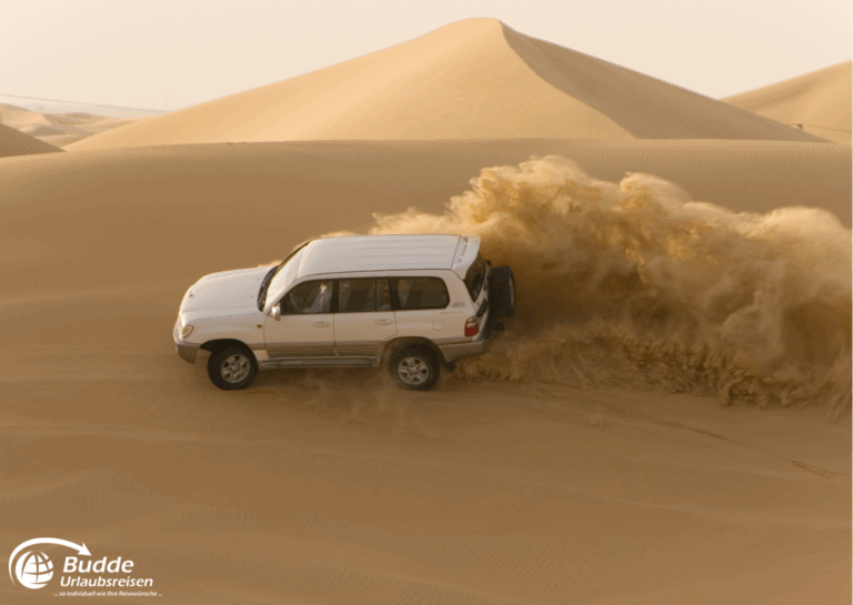 einzigartige Reiseerlebnisse weltweit: Ein Geländewagen fährt durch den Sand in einer Wüstenlandschaft und wirbelt Staub auf. - buchbar im Reisebüro Budde Urlaubseisen