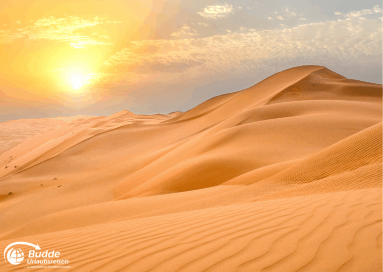 einzigartige Reiseerlebnisse weltweit: Sanddünen in einer Wüste mit Sonnenuntergang im Hintergrund und Wolken am Himmel. - buchbar im Reisebüro Budde Urlaubseisen