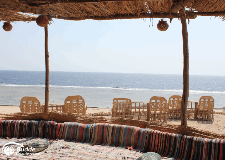 einzigartige Reiseerlebnisse weltweit: Sitzbereich mit bunten Teppichen und Blick auf das Meer, umgeben von Stühlen aus Rattan. - buchbar im Reisebüro Budde Urlaubseisen