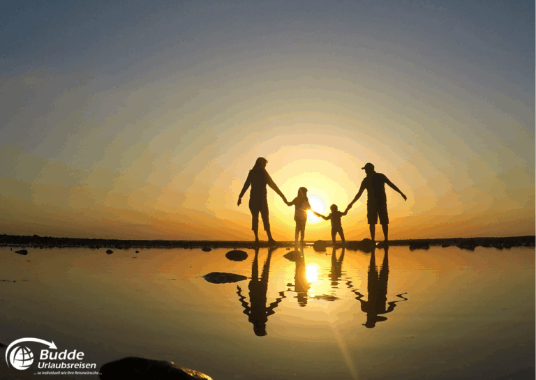 Langzeiturlaub buchen: Familie hält sich an den Händen und steht im Wasser während des Sonnenuntergangs am Strand. - buchbar im Reisebüro Budde Urlaubseisen