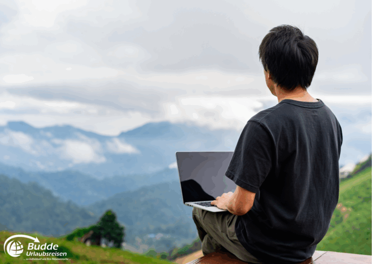 Langzeitreise buchen: Mann sitzt mit einem Laptop in der Natur und blickt auf eine Berglandschaft mit Wolken. - buchbar im Reisebüro Budde Urlaubseisen