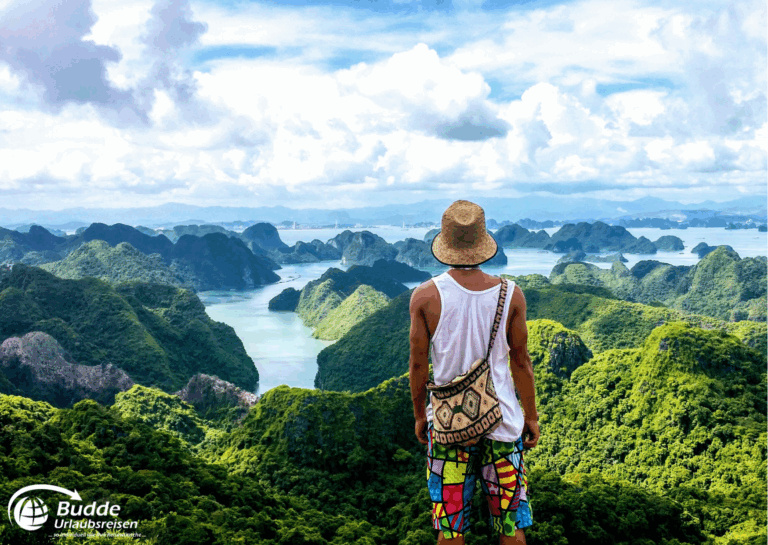 Langzeitreise buchen: Mann mit Hut und bunten Shorts steht vor einer Aussicht auf grüne Hügel und Gewässer in Vietnam. - buchbar im Reisebüro Budde Urlaubseisen