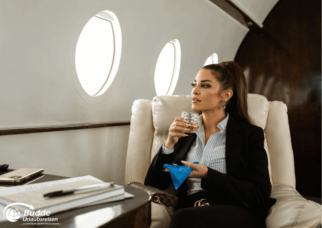 Frau sitzt in einem Privatjet und hält ein Glas mit Getränk in der Hand. - Dein Luxusurlaub buchbar im Reisebüro Budde Urlaubseisen