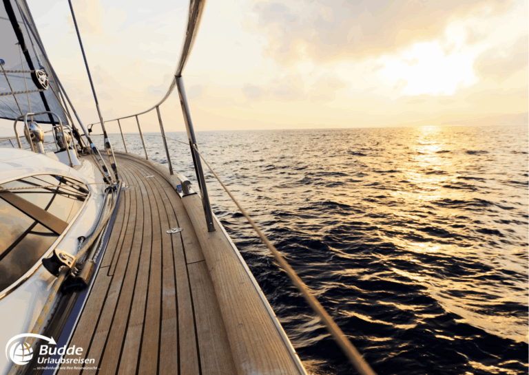 Yacht mit Holzdeck, die auf ruhigem Wasser bei Sonnenuntergang fährt. - buchbar im Reisebüro Budde Urlaubseisen