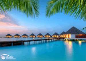 Wasserbungalows in den Malediven bei Sonnenuntergang mit ruhigem Wasser im Vordergrund. - buchbar im Reisebüro Budde Urlaubseisen
