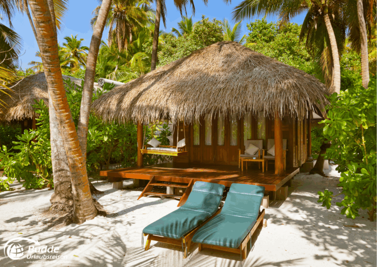 Ein Strandbungalow mit Strohdach und Liegen auf einer tropischen Insel. - buchbar im Reisebüro Budde Urlaubseisen