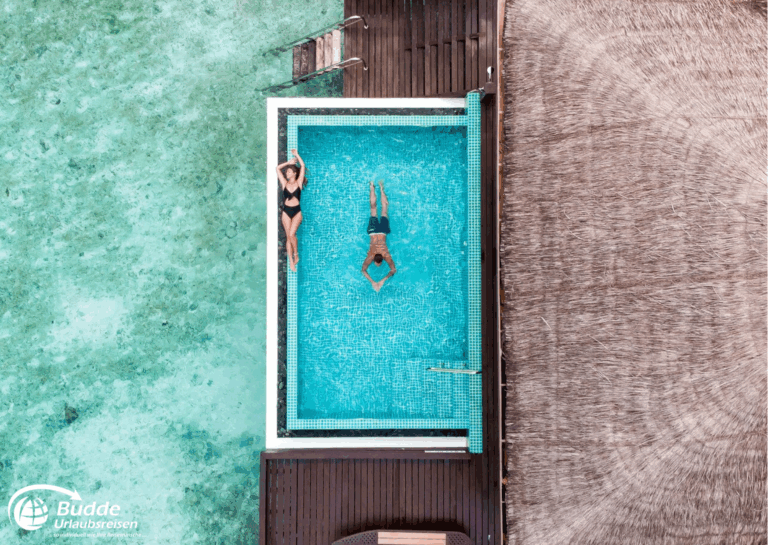 Zwei Personen schwimmen in einem Pool auf den Malediven, umgeben von Wasser und Holzdeck. - buchbar im Reisebüro Budde Urlaubseisen