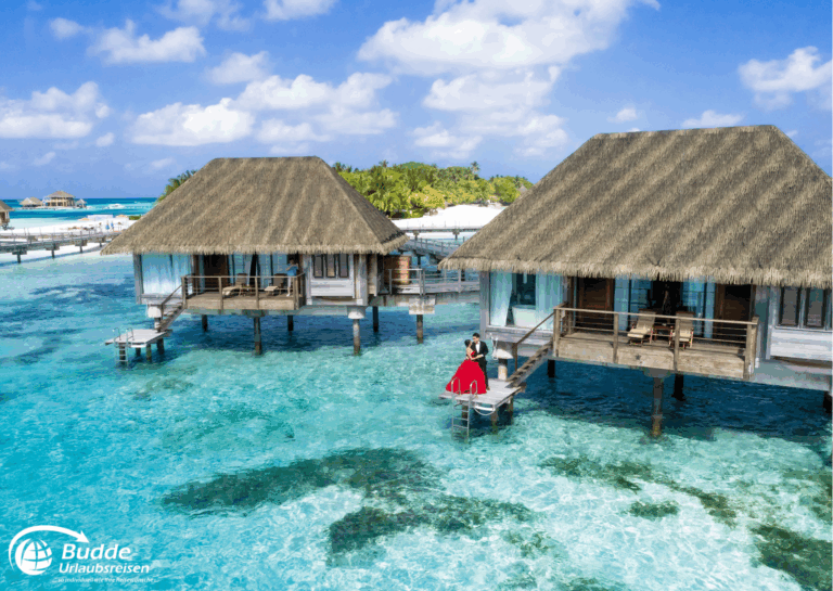 Zwei Überwasser-Bungalows auf den Malediven mit klaren Wasser und einer Person in rotem Kleid. - buchbar im Reisebüro Budde Urlaubseisen