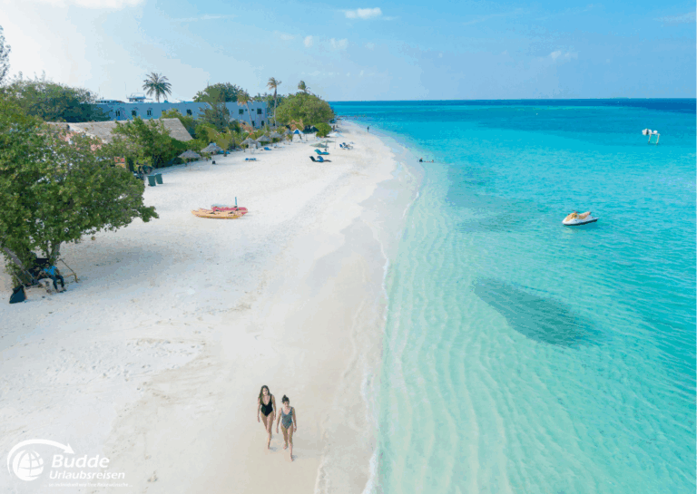 Zwei Personen gehen am Strand entlang, umgeben von klarem Wasser und feinem Sand in den Malediven. - buchbar im Reisebüro Budde Urlaubseisen