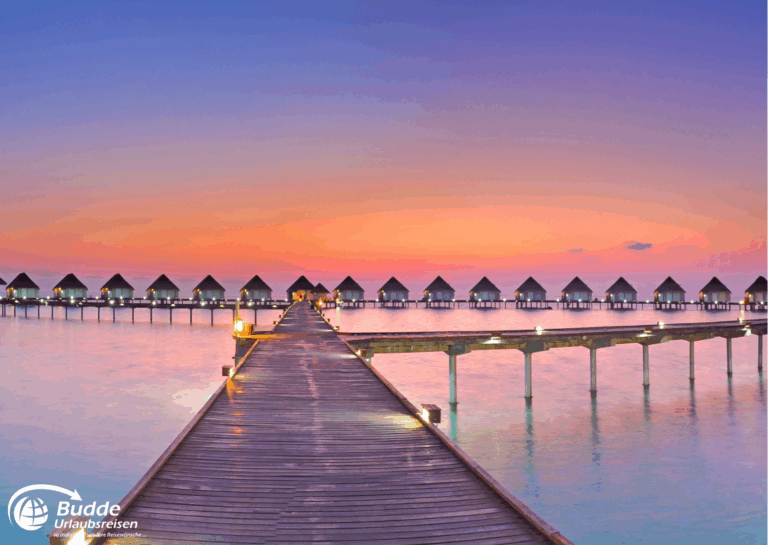 Holzsteg, der zu Wasserbungalows führt, unter einem bunten Sonnenuntergang am Meer. - buchbar im Reisebüro Budde Urlaubseisen