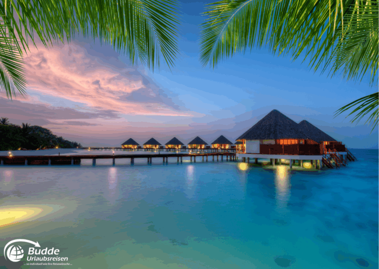 Wasserbungalow auf den Malediven mit Holzsteg und tropischer Umgebung bei Sonnenuntergang. - buchbar im Reisebüro Budde Urlaubseisen