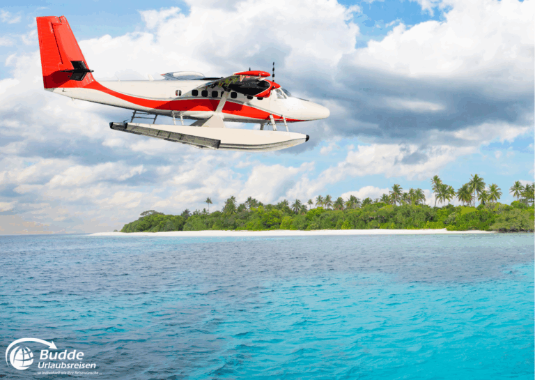 Ein Wasserflugzeug fliegt über das blaue Wasser des Ozeans in der Nähe einer tropischen Insel. - buchbar im Reisebüro Budde Urlaubseisen